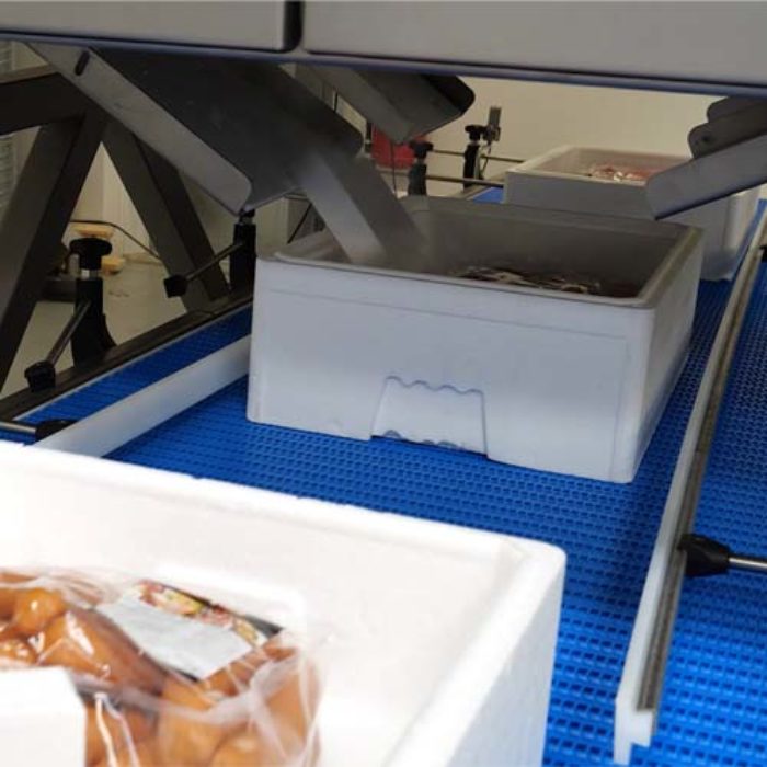 Automatisierte Befüllung von Styroporboxen mit Trockeneis zur Kühlung von Lebensmitteln wie verpackten Würstchen auf einem Förderband in einer Lebensmittelverpackungslinie.